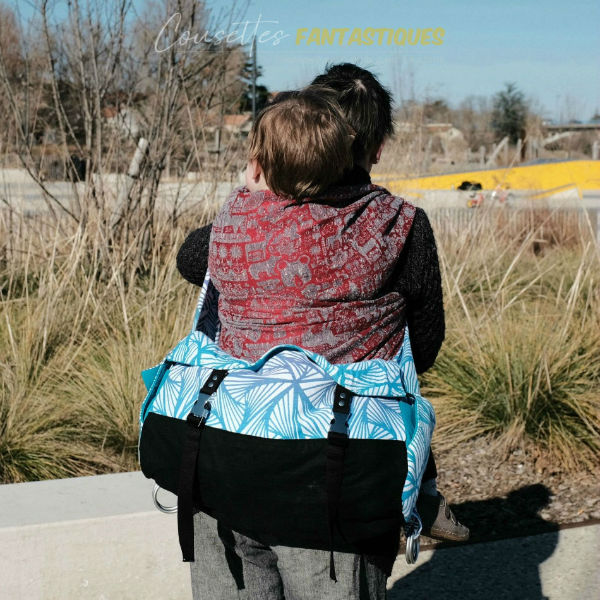 Blue babywearing bag in Crossbody style, in the back, baby on back. Picture taken outside.