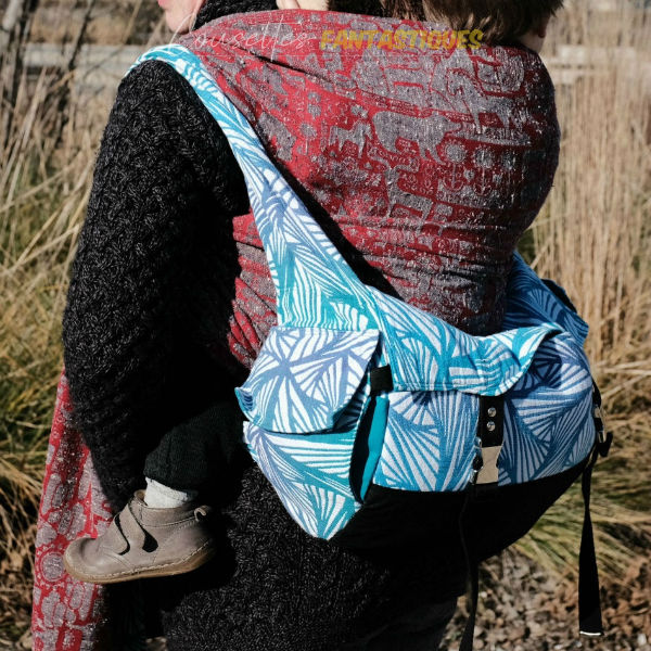 Sac de portage bleu en mode sac à dos, vue de dos, bébé au dos. Photo prise en extérieur.