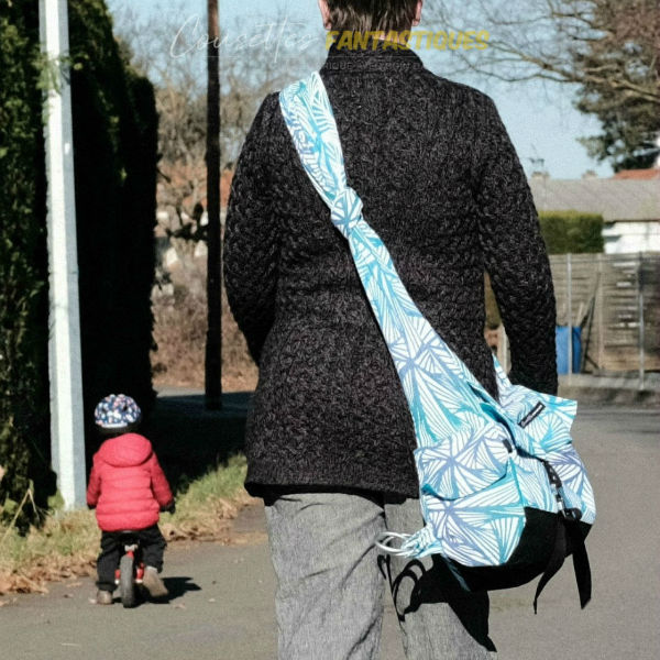Blue babywearing bag in Crossbody style, adjustable straps, without baby. Picture taken outside.