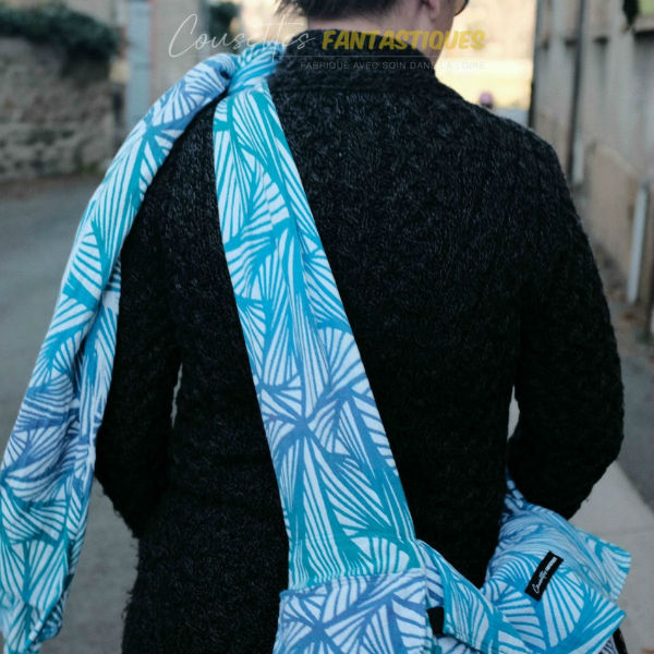 Blue babywearing bag in Crossbody style, fixed straps, without baby. Picture taken outside.