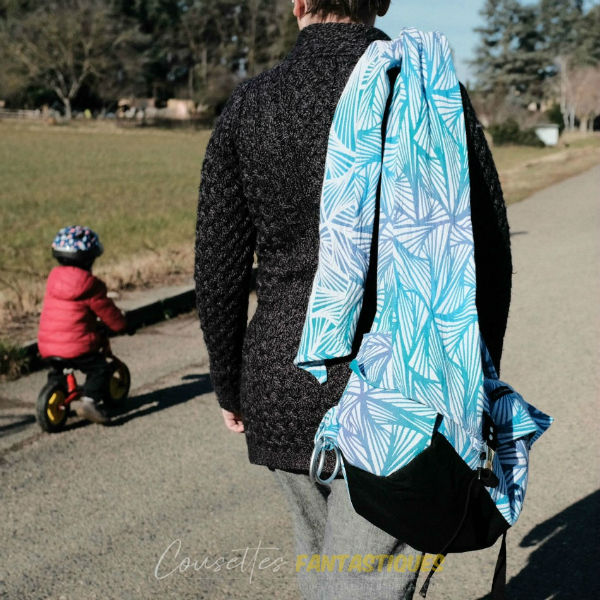 Blue babywearing bag in shoulder bag style, without baby. Picture taken outside.