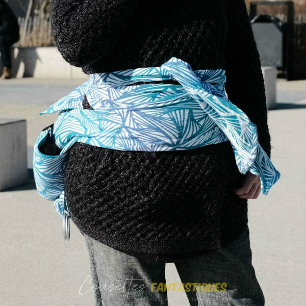 Sac de portage bleu en mode 'pagne' sans les anneaux, finition 'belly wrapping', sans bébé. Photo prise en extérieur.