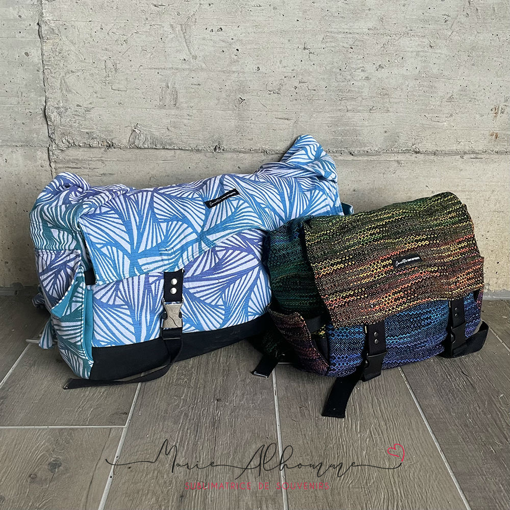 Two babywearing bags next to each other, the big one is blue while the other is a dark rainbow